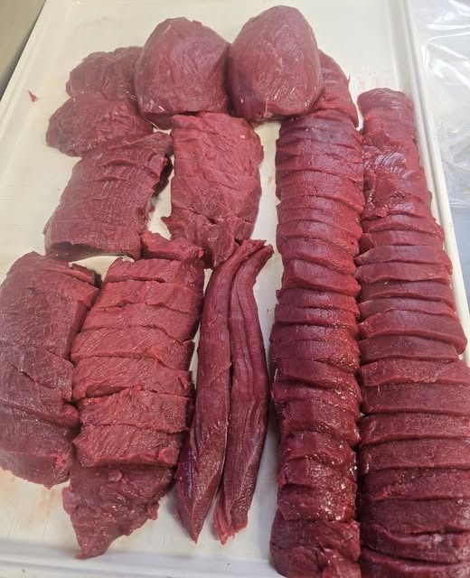 Trimmed venison on a white cutting board, including roasts, sliced steaks and two tenderloins