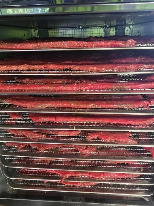 Thin strips of meat laid out on stainless-steel drying racks