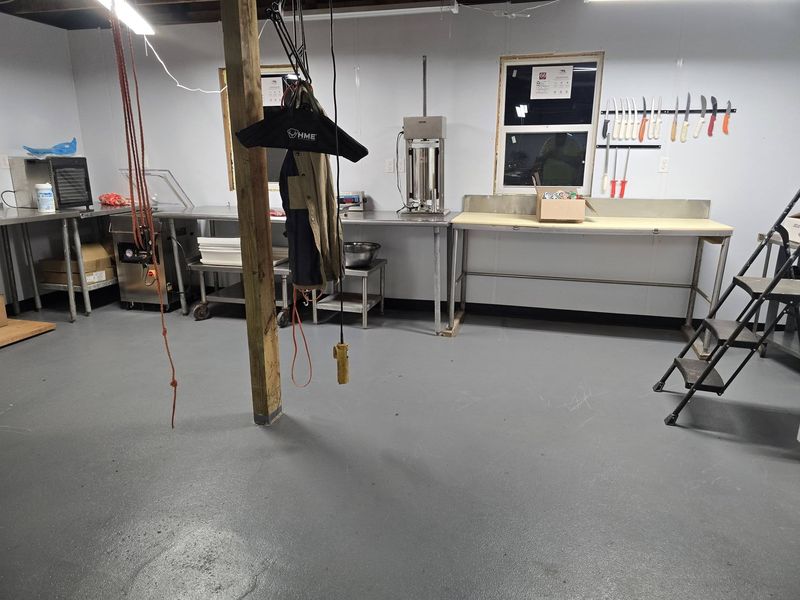 Wide view of the processing room with stainless-steel work tables, a sausage stuffer, a knife rack and an overhead hoist